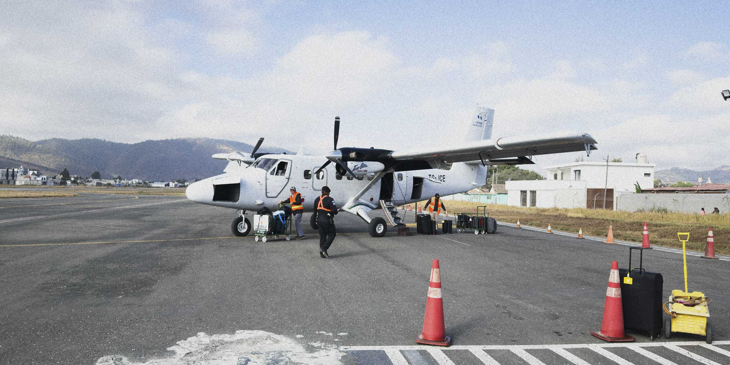 Small propeller airplane on a runway with ground crew and equipment.