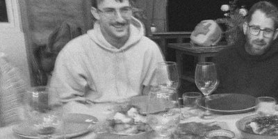 Two men sitting at a table with food and drinks, black and white photo.