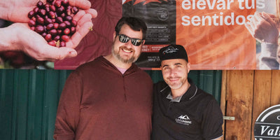 Two men standing in front of a promotional banner with coffee beans and text.