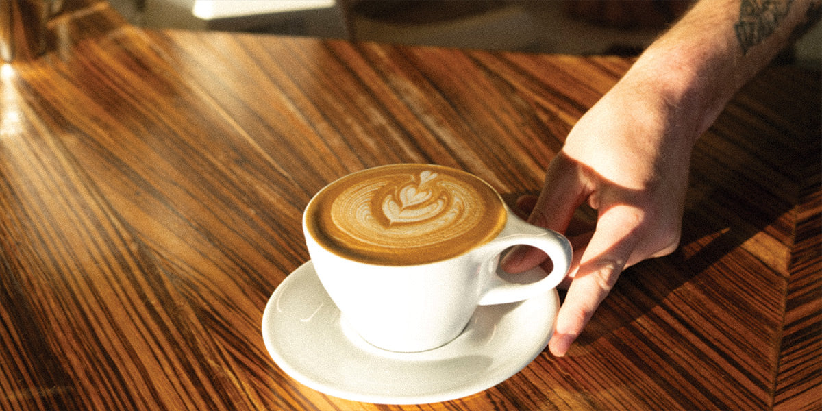 Hand holding a cup of cappuccino with latte art on a wooden table