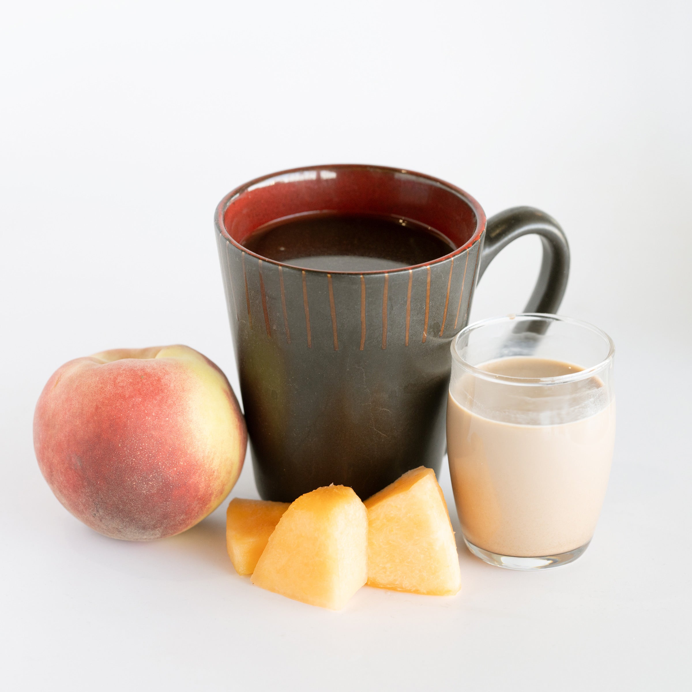 Mug of coffee with peach, cantaloupe pieces, and glass of chocolate milk on a white background