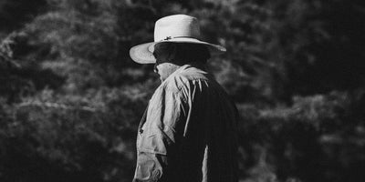 Edwin wearing a wide-brimmed hat and jacket standing in a forest