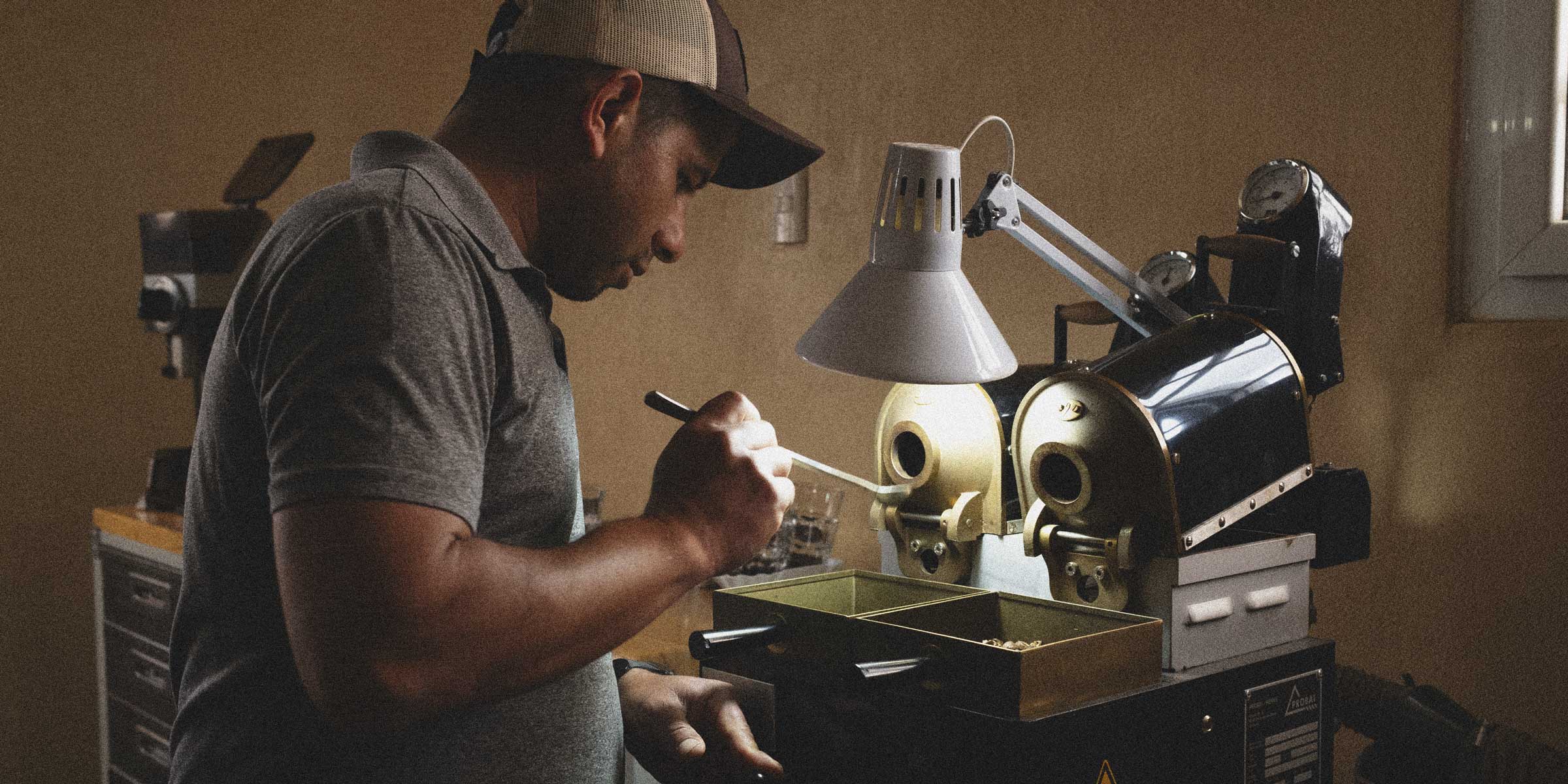 Man working on a coffee sample roaster with a lamp in a workshop setting