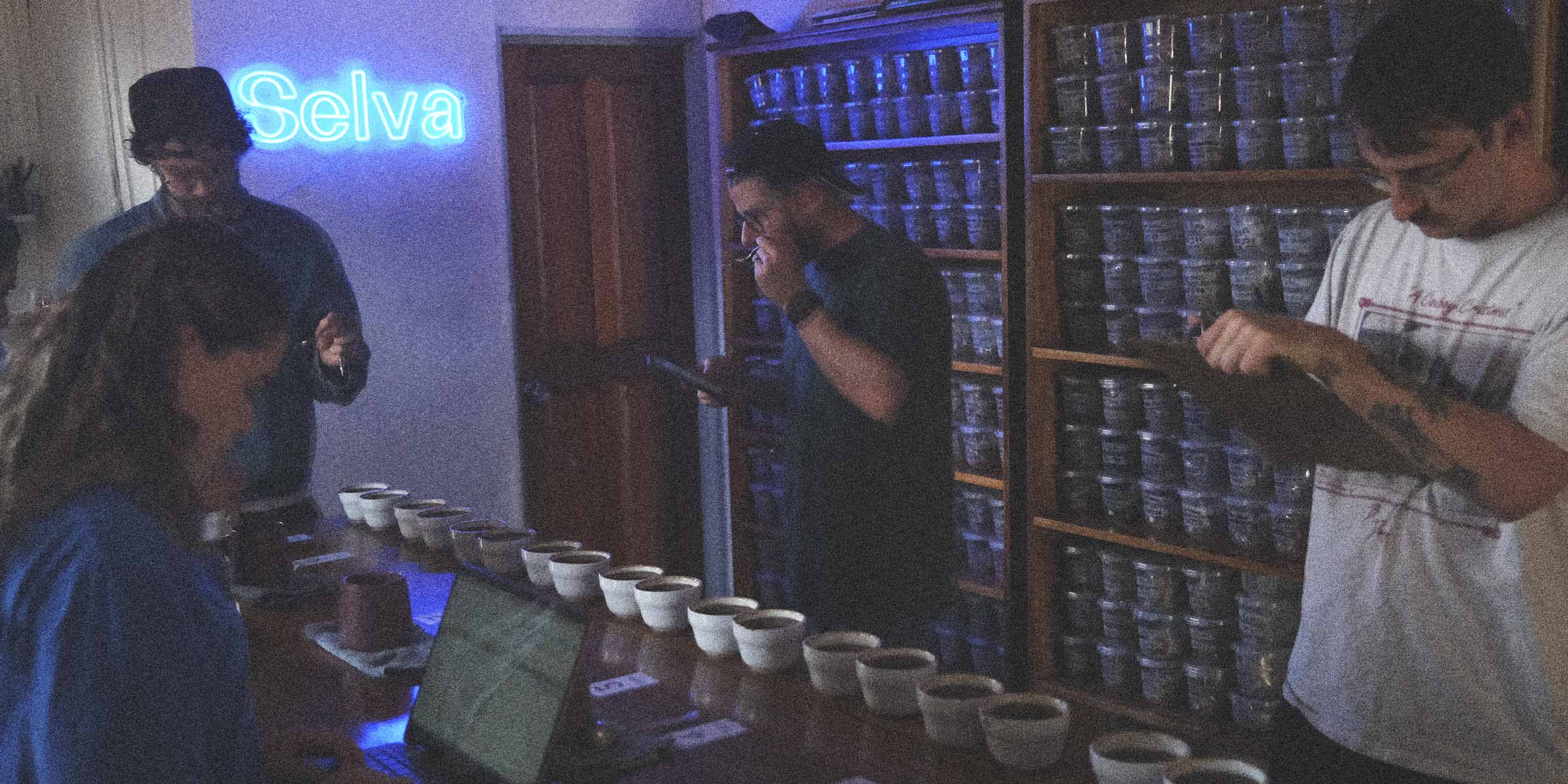 Multiple people cupping specialty coffee in a room with a neon sign