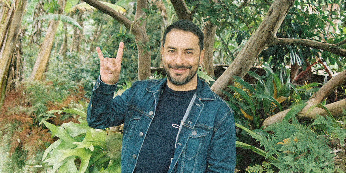 Man in a denim jacket making a "rock on" gesture in a specialty coffee farm