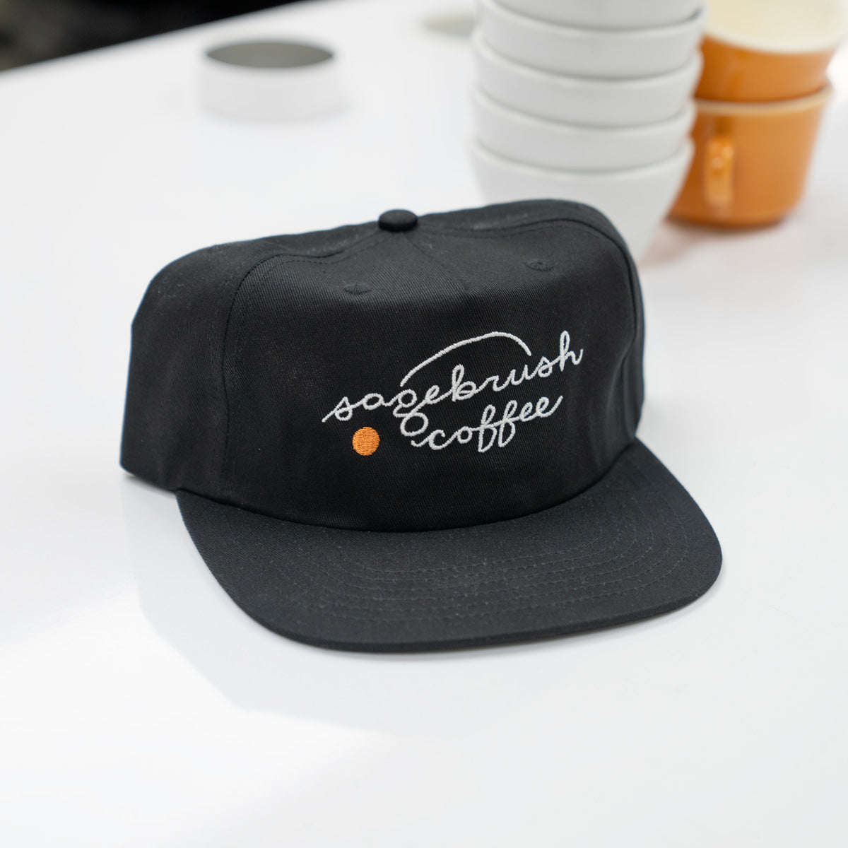 Black cap with 'sagebrush coffee' embroidery on a white surface