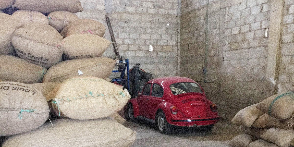 Red vintage car parked inside a warehouse with stacked burlap sacks.