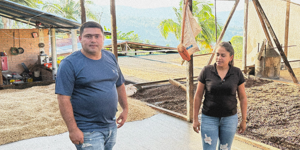 Gildardo and his wife talking about coffee as they stand among coffee on drying beds
