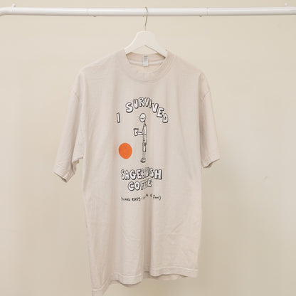 Beige t-shirt with graphic design on a hanger against a beige wall