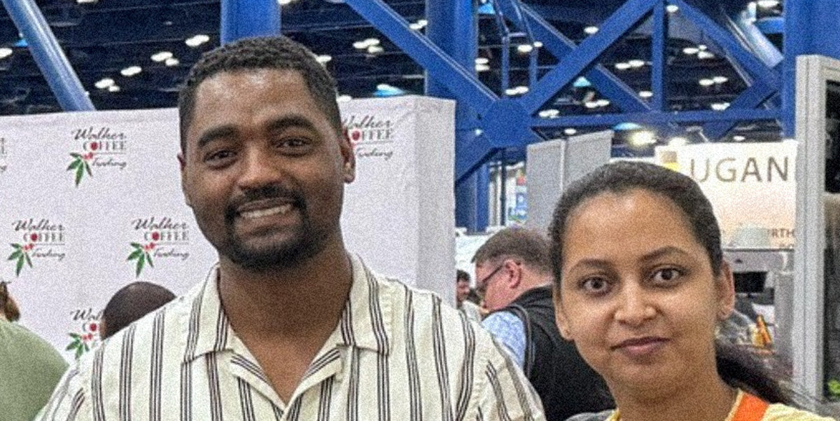 Two people standing in front of a branded backdrop at a specialty coffee convention