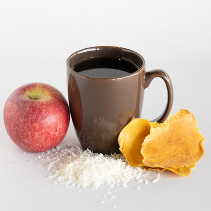 Brown mug with coffee, a red apple, coconut, and dried mango on a white background