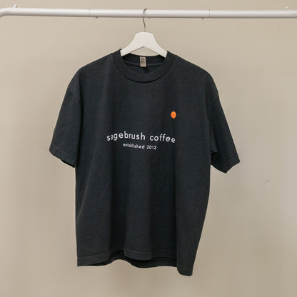 Black t-shirt with 'sagebrush coffee' text on a hanger against a beige background