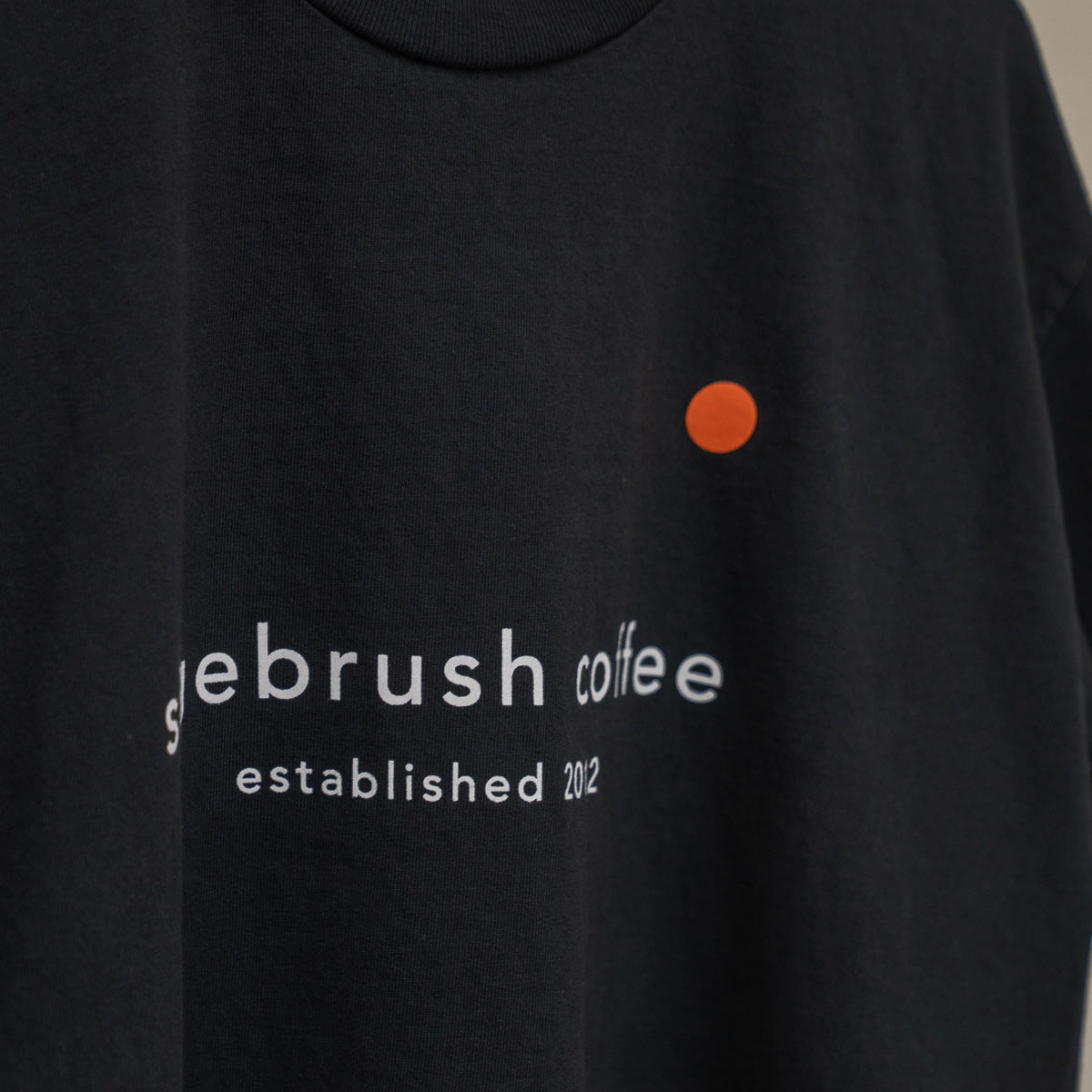 Black shirt with 'sagebrush coffee' text and an orange dot on a beige background